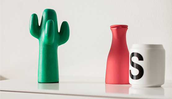 Ein grüner Deko-Kaktus mit einer roten Vase und einer Tasse mit aufgedrucktem „S“