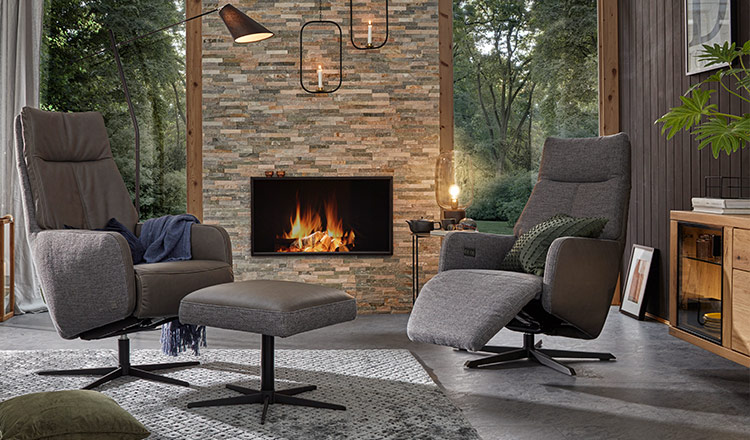 Ein grauer Sessel mit Relaxfunktion und einer mit dem passenden Hocker vor einem Kamin