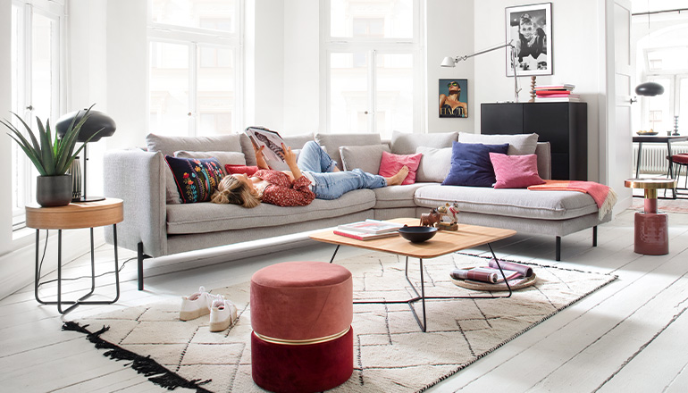 Rosafarbener Hocker im modernen Wohnzimmer mit grauem Sofa und schwarzer Kommode