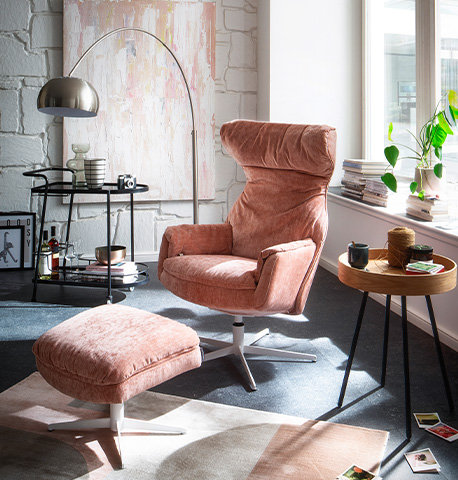 Rosa Sessel mit passendem Hocker, beides drehbar und mit weißem Gestell, im hellen Wohnzimmer mit Teppich, Barwagen und Beistelltisch