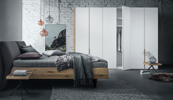 Schlafzimmer mit Bett aus Massivholz vor weißem Kleiderschrank