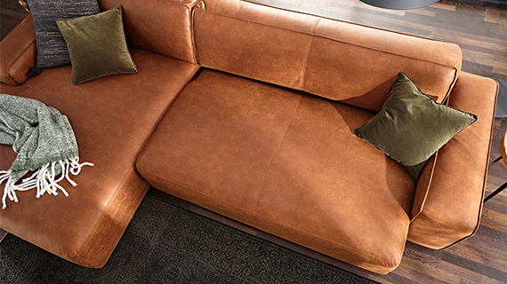Hellbraune Couch aus glattem Leder mit Kissen und Decke