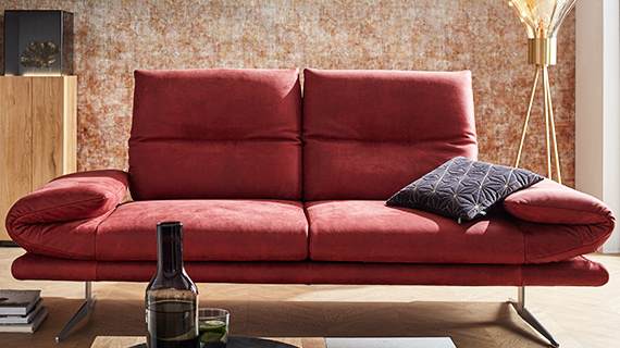 Rotes 2-Sitzer Sofa aus Rauleder mit filigranen Füßen vor einer rostbraunen Wand